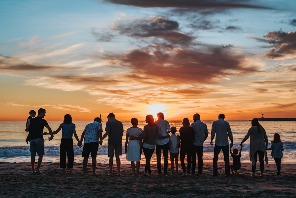 Família reunida de mãos dadas na beira do mar ao pôr do sol
